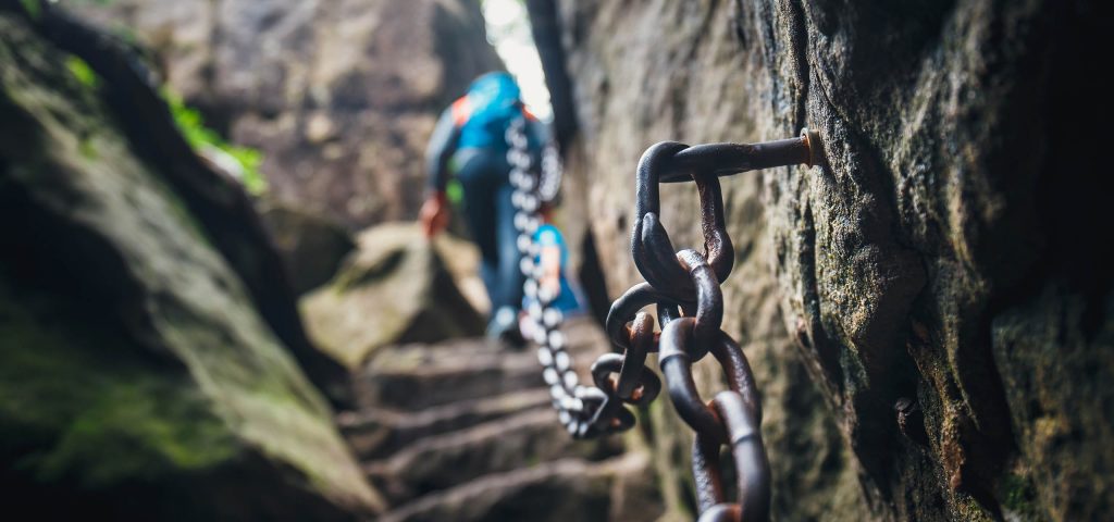 A person walking along a rock face with a chain attached to it