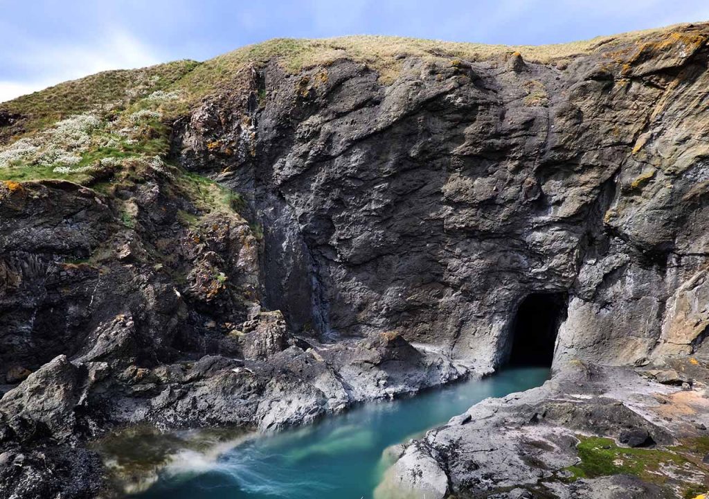 A cliff face with a cove and blue waters at Elie Chain Walk in Fife