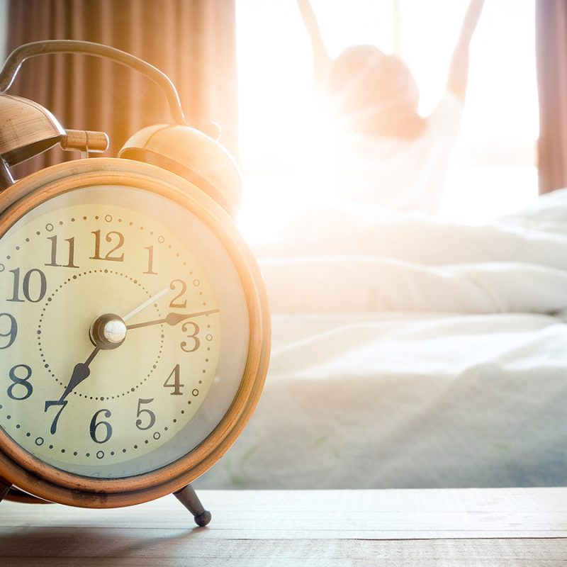A picture of a clock with someone getting out of bed in the morning and stretching their arms up in the air