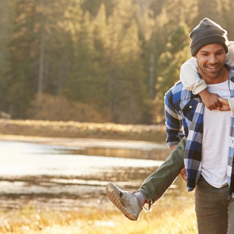 Parents Giving Children Piggyback Ride On Walk By Lake on holiday