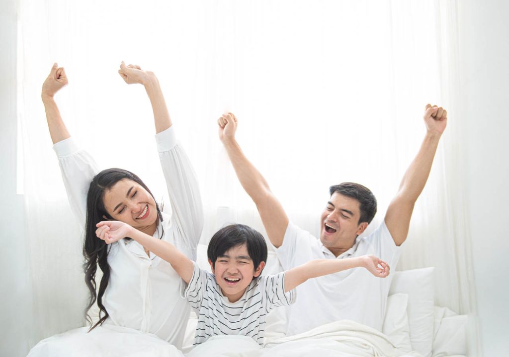 A happy family having a stretch when they wake up together on holiday.