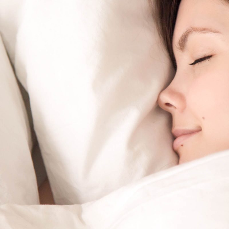 A smiling lady asleep on a comfy pillow.