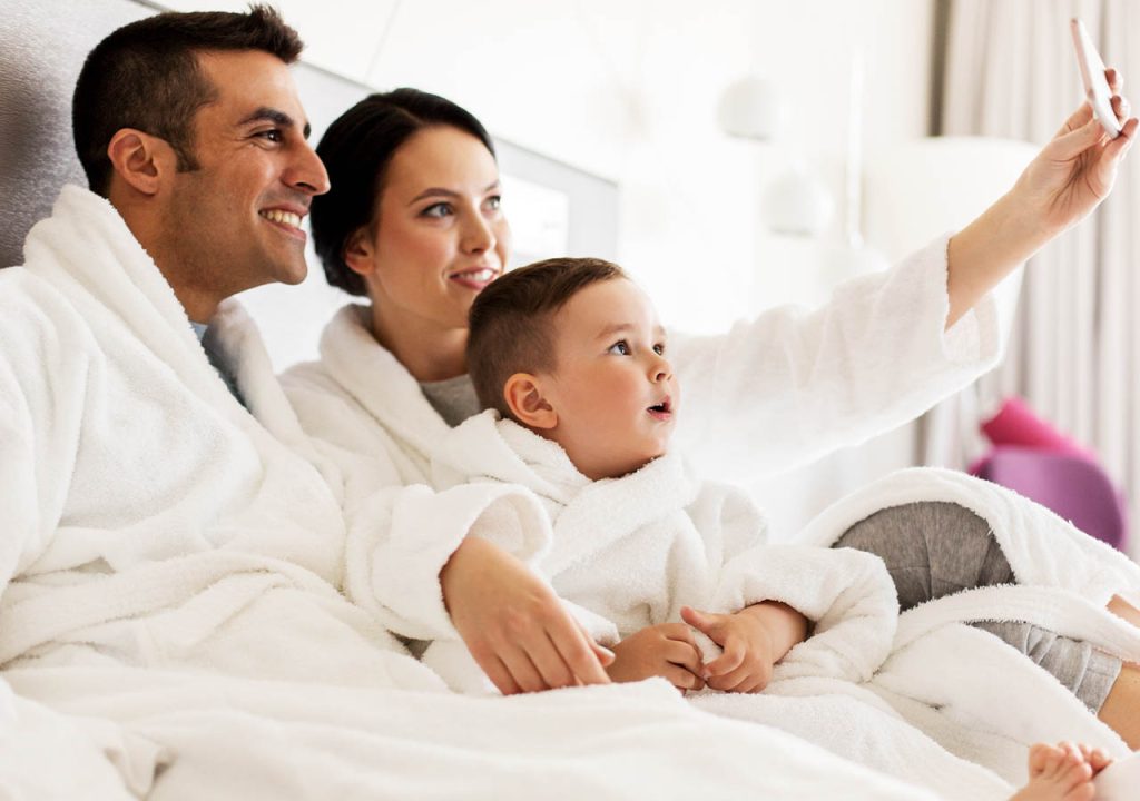 A family on holiday in their pajamas taking a selfie on bed.