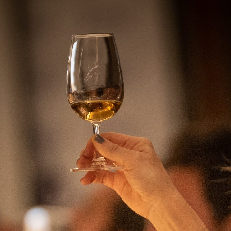 Woman holding up a dram of whisky on a tasting
